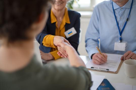 Woman and man volunteers helping Ukrainian woman to fill in forms at asylum centre.